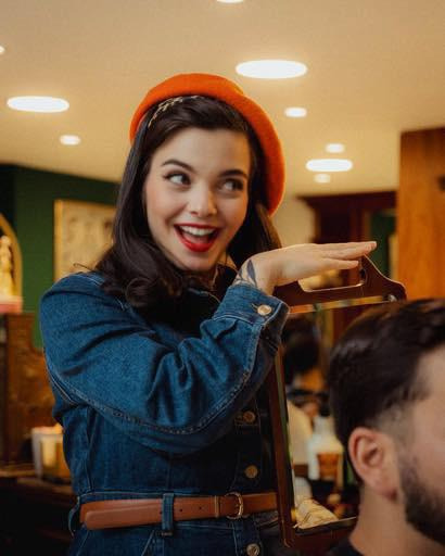 Jean in denim and beret holds Olivia Garden mirror, showcasing premium styling tools inspiration in warmly lit salon.